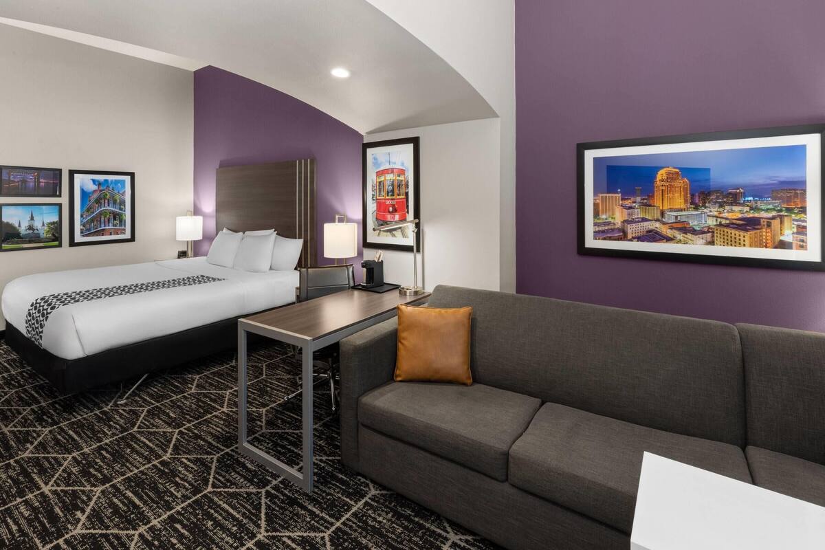 Una habitación de hotel con cama, sofá, escritorio y cuadros en las paredes.