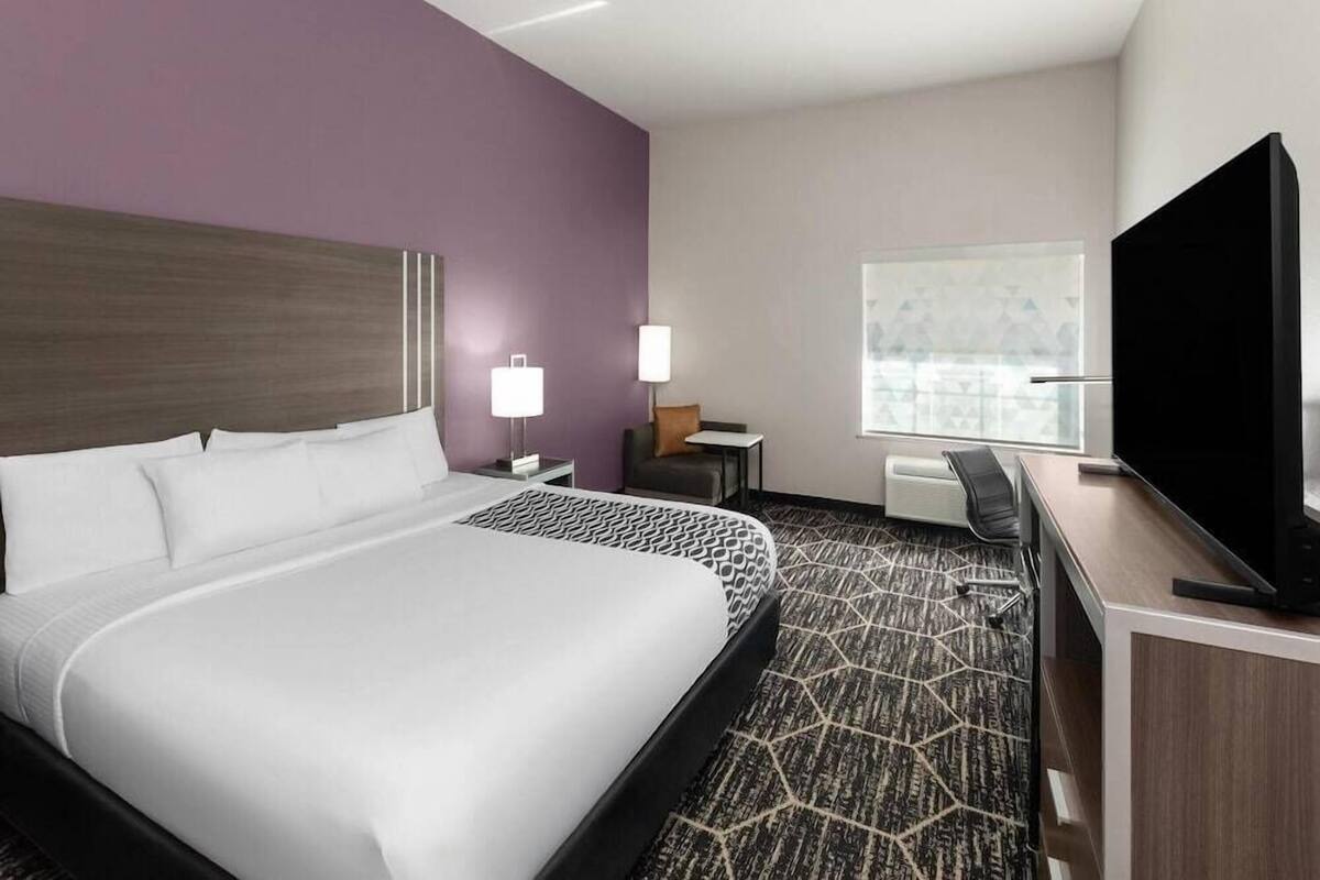 Habitación de hotel con una cama grande, un escritorio con televisor de pantalla plana, una silla, una lámpara y una ventana con vistas.
