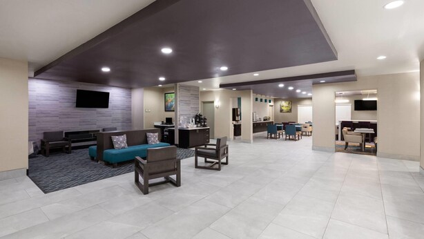 A spacious lobby with a modern design, featuring a seating area with sofas and chairs, a reception desk, and a flat-screen TV mounted on the wall. - La Quinta Inn & Suites by Wyndham Boutte (Boutte)