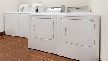 A row of white front-loading washers and dryers in a laundry room with wooden flooring.