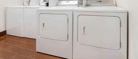A row of white front-loading washers and dryers in a laundry room with wooden flooring.