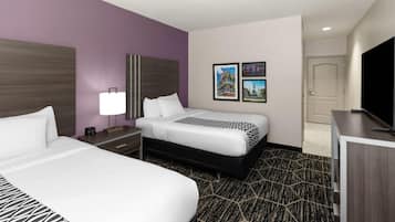 A hotel room with two beds, a desk, a TV, and a door.