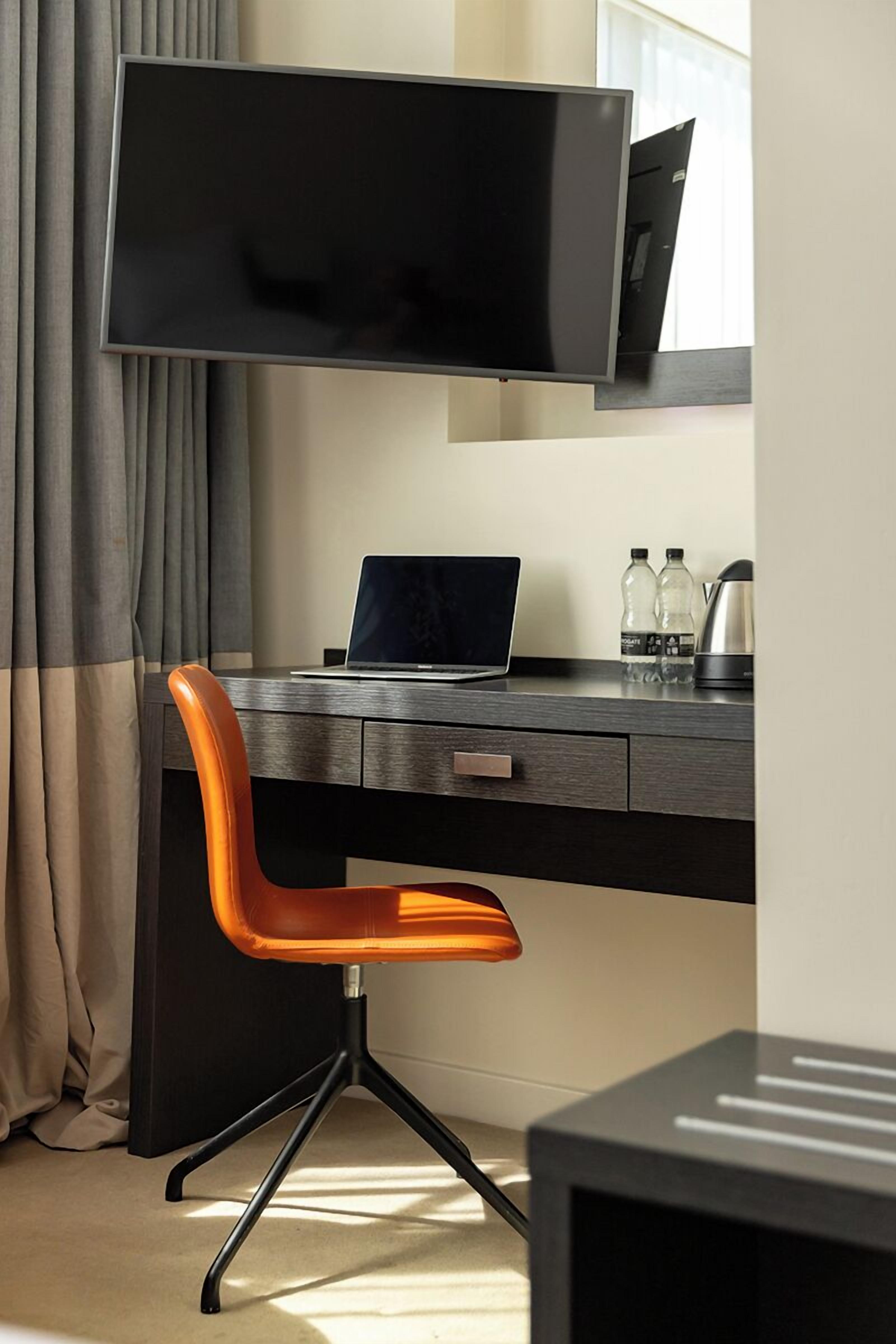 Un espace de bureau moderne comprenant un bureau, une chaise, un ordinateur portable et un grand téléviseur à écran plat fixé au mur.