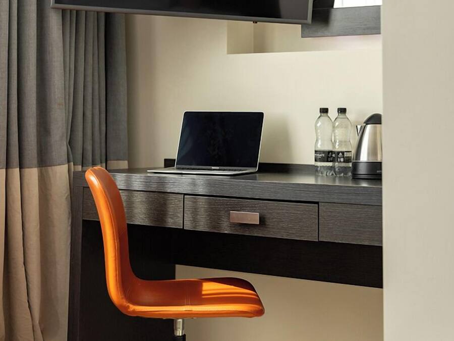 Un espace de bureau moderne comprenant un bureau, une chaise, un ordinateur portable et un grand téléviseur à écran plat fixé au mur.