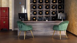 Zona de recepción con un escritorio de madera, dos sillas verdes con patas doradas, un armario rojo y una pared decorada con esferas.