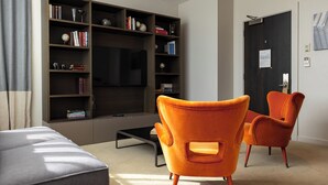 Una sala de estar moderna con una amplia estantería, dos sillones anaranjados, un sofá gris y un televisor de pantalla plana.