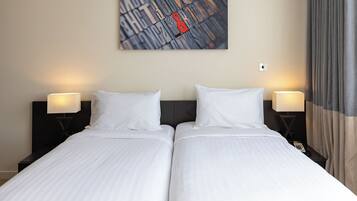 A hotel room with two single beds, a nightstand with a lamp, and a wall-mounted artwork.