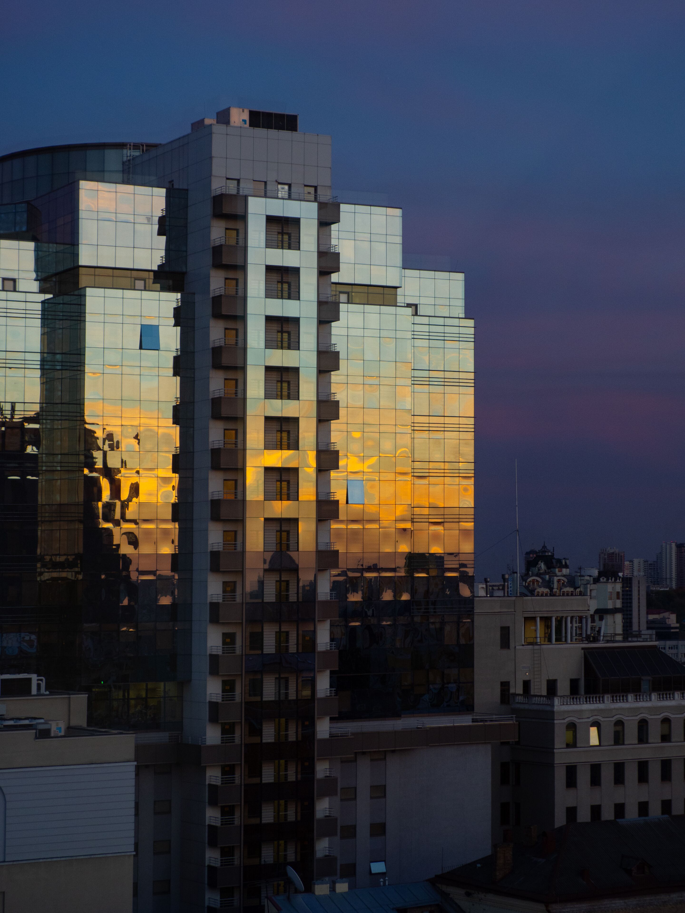 A high-rise building with a reflective glass facade, multiple balconies, and a mix of architectural styles.