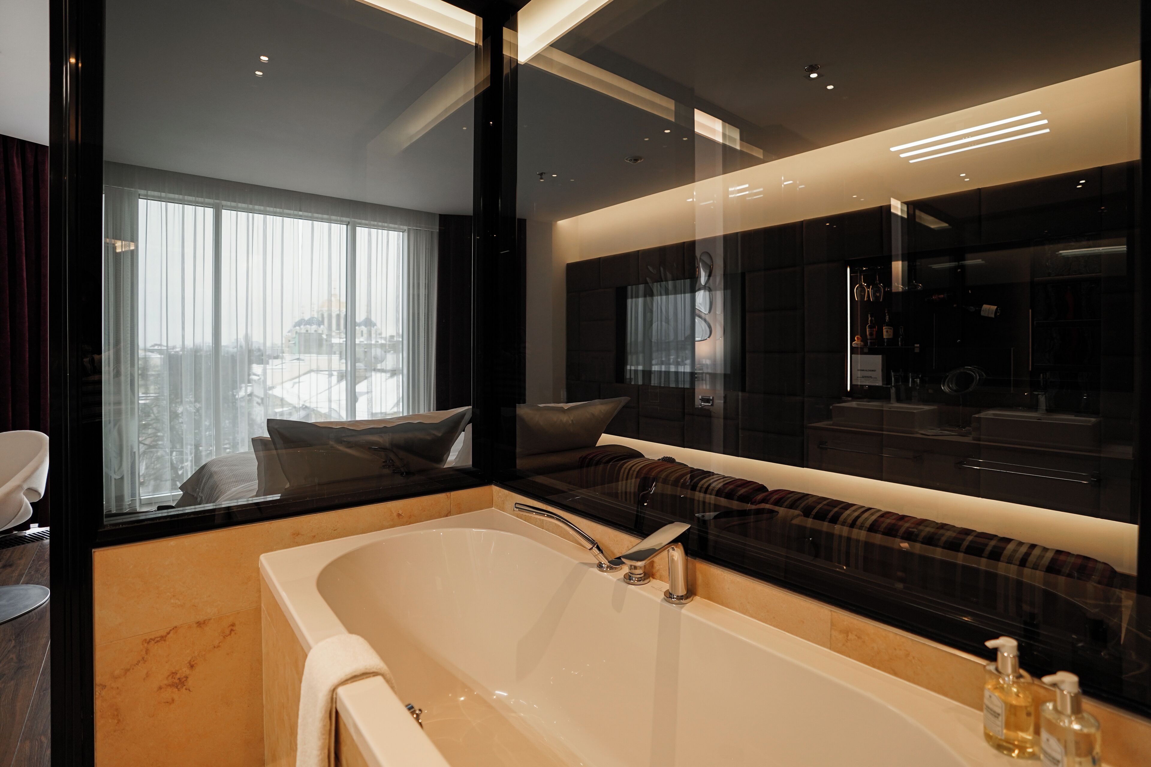 A modern bathroom with a large bathtub, a vanity with a mirror, and a view of the city through large windows.