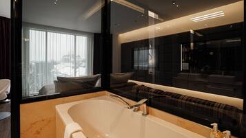 A modern bathroom with a large bathtub, a vanity with a mirror, and a view of the city through large windows.