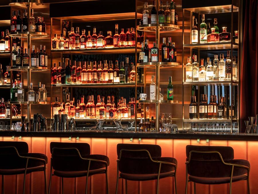 A bar area with multiple shelves of liquor bottles, a bar counter, and seating with tables and chairs.