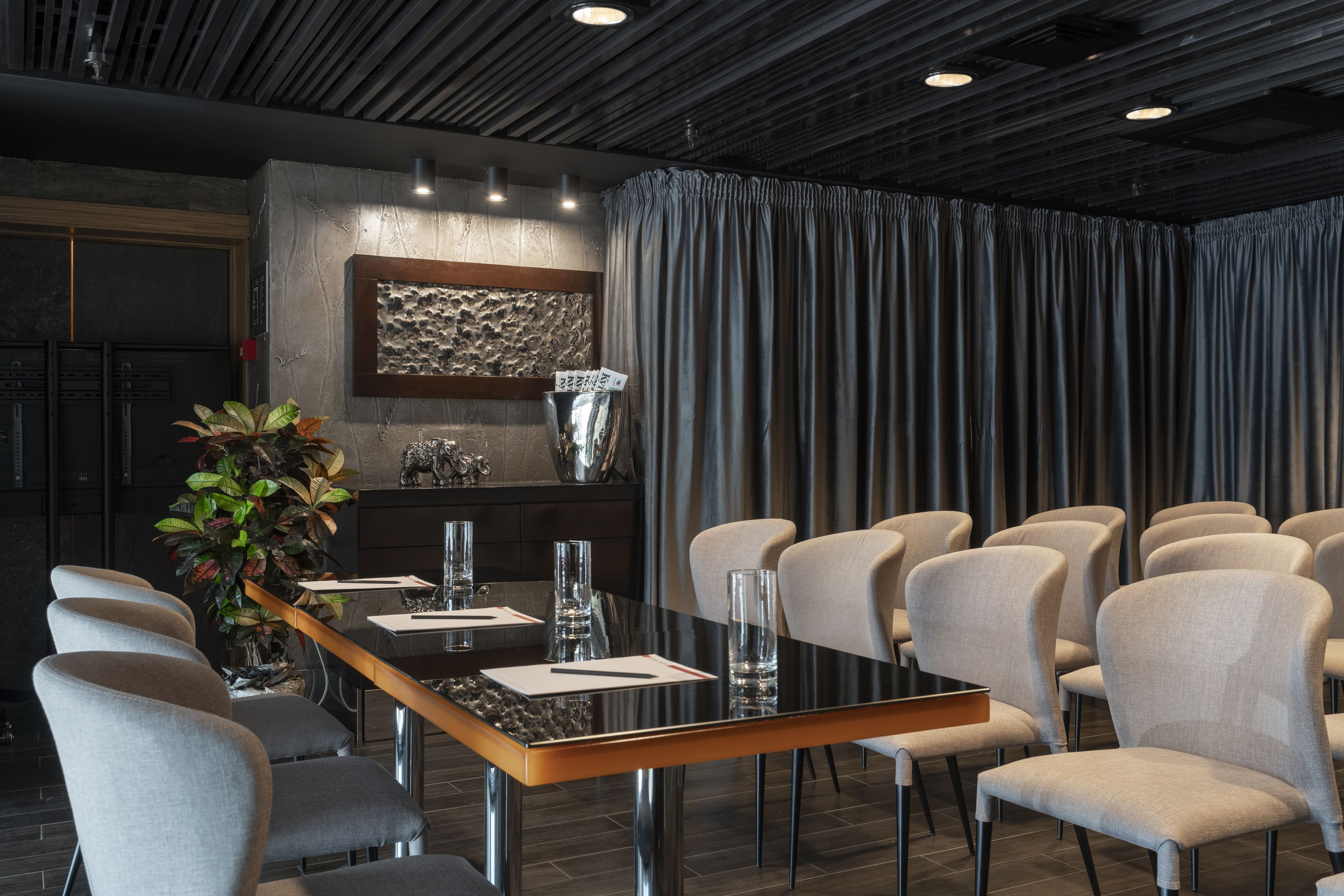 A modern conference room with a long table, several chairs, a decorative plant, and a textured wall art piece.