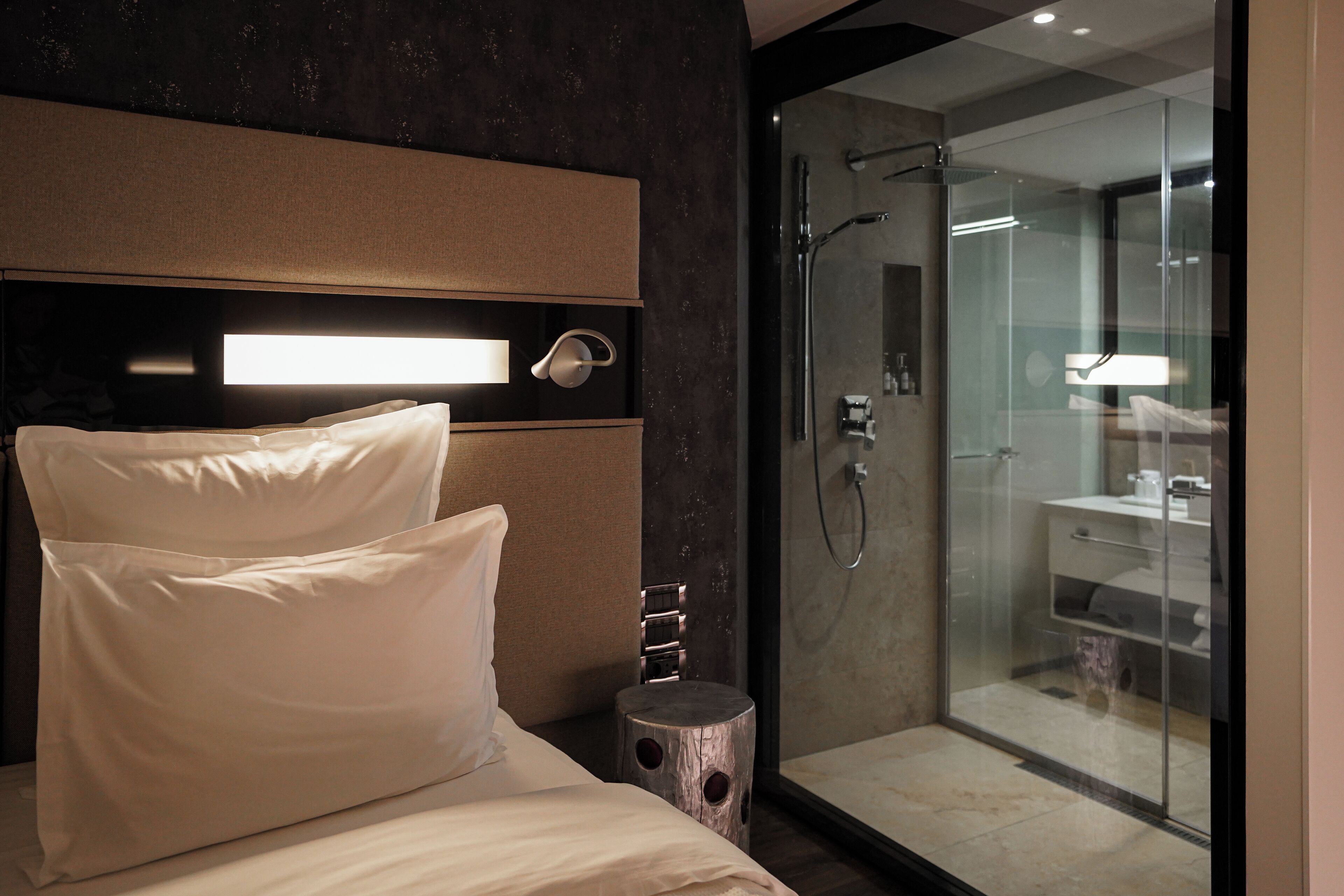 Una habitación de hotel moderna con una cama grande, una mesita de noche y un área de ducha con mampara de vidrio.
