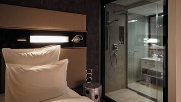 Una habitación de hotel moderna con una cama grande, una mesita de noche y un área de ducha con mampara de vidrio.