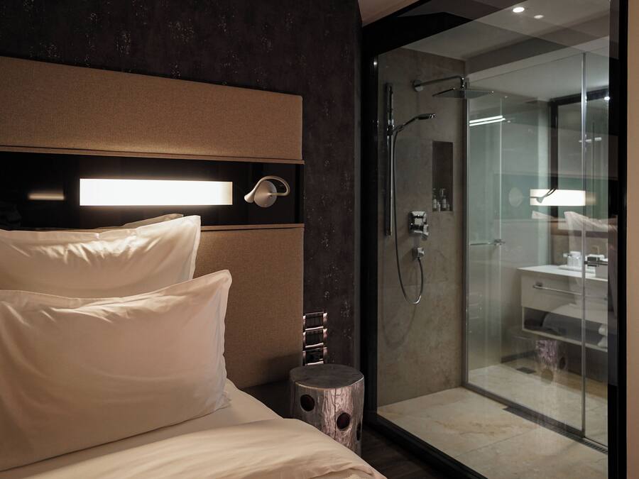 Una habitación de hotel moderna con una cama grande, una mesita de noche y un área de ducha con mampara de vidrio.