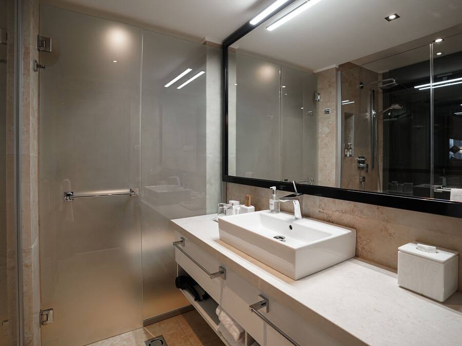 A modern bathroom with a glass shower enclosure, a large mirror, and a white sink with a vanity.