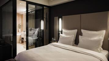 Una habitación de hotel moderna con una cama grande, un baño con paredes de vidrio y un escritorio con una silla.