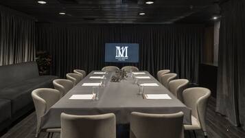 Une salle de conférence avec une longue table, des chaises, un canapé et un écran affichant le logo.