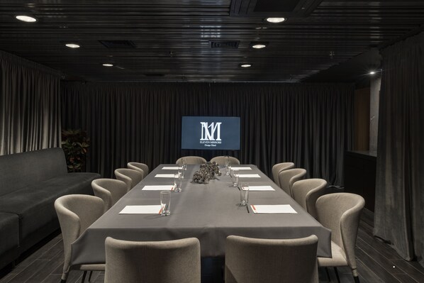 A conference room with a long table, chairs, a sofa, and a screen displaying the logo.