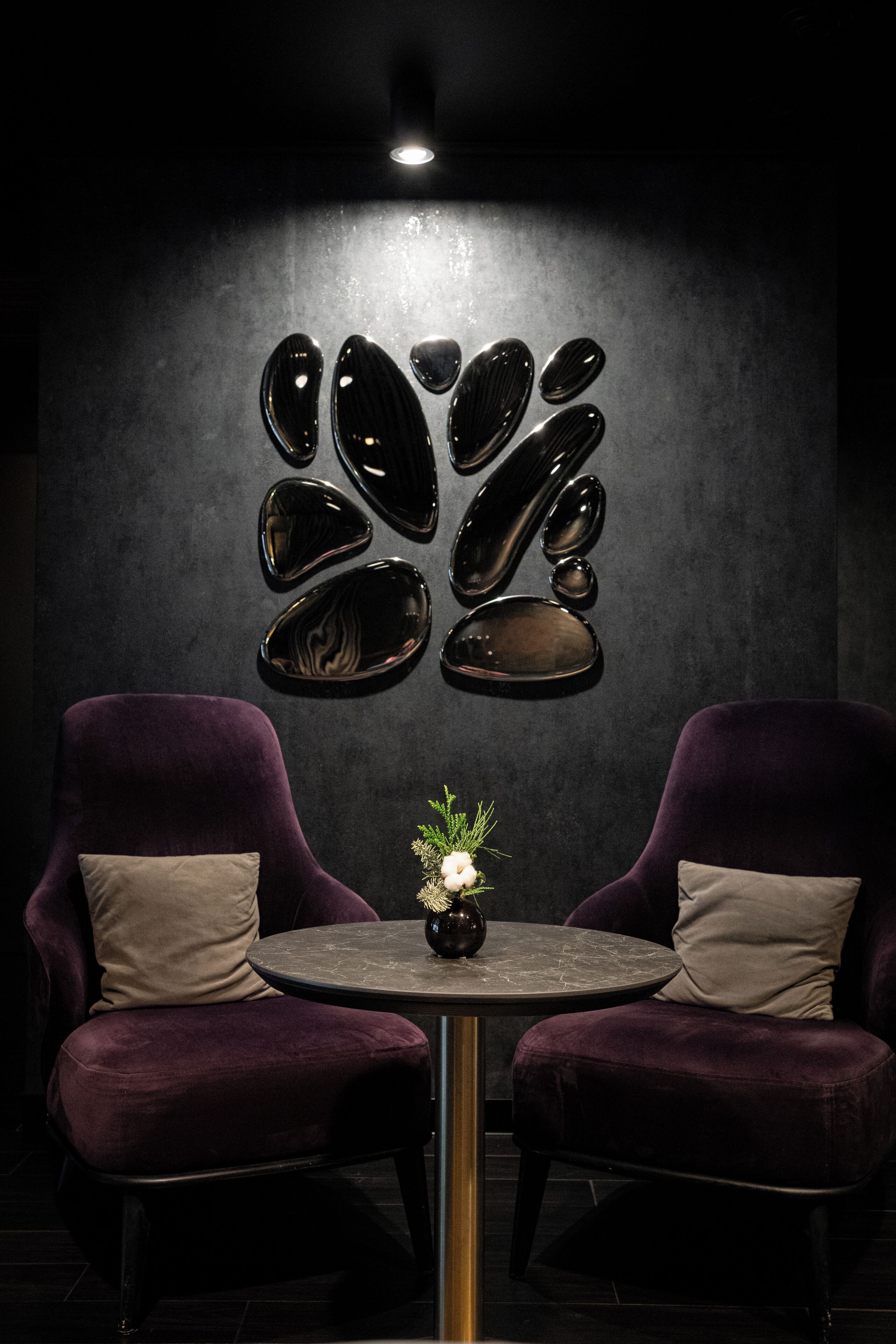 Una habitación con dos sillones morados, una mesita con un florero y una pared decorada con obras de arte reflectantes.
