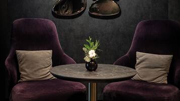 Una habitación con dos sillones morados, una mesita con un florero y una pared decorada con obras de arte reflectantes.