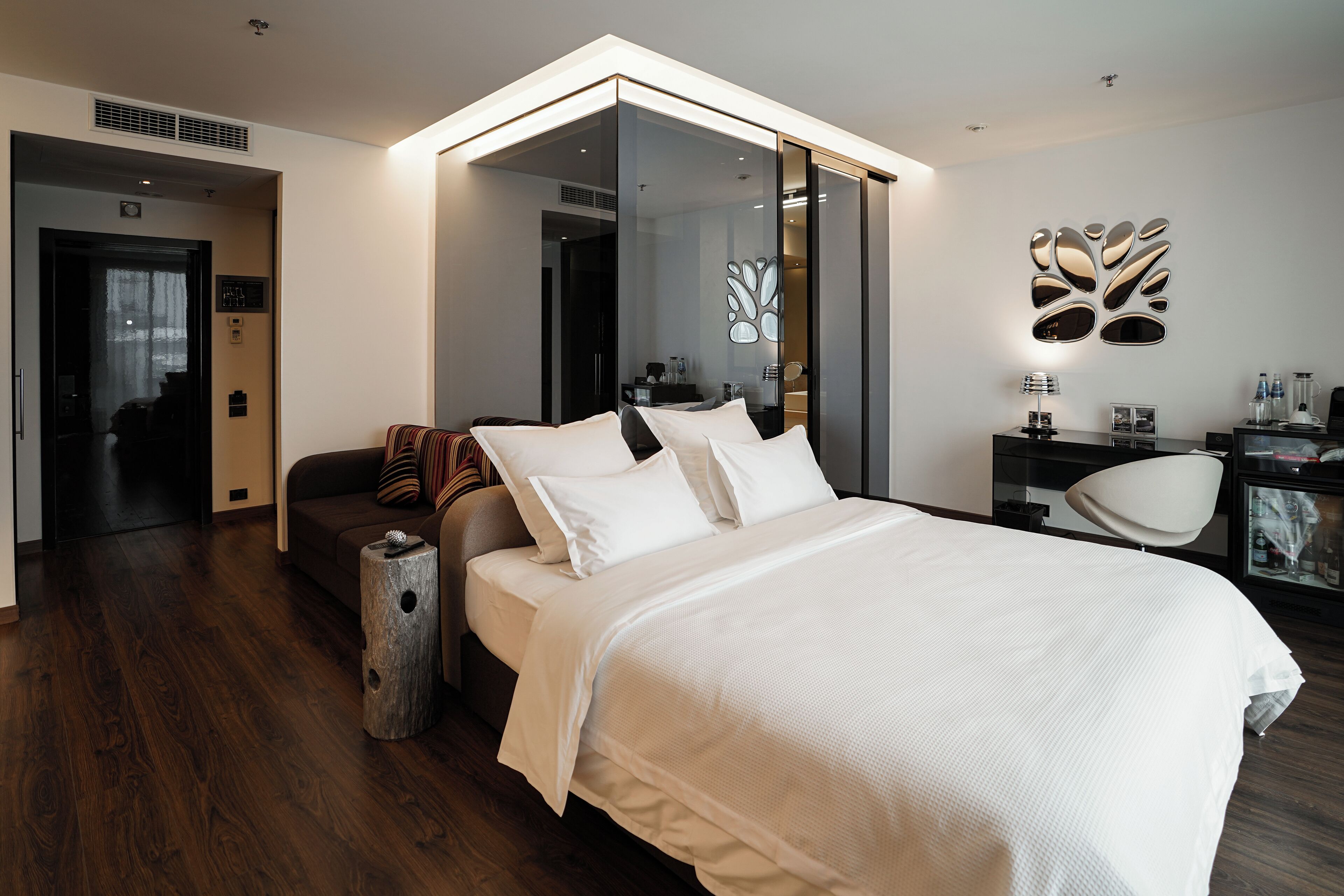 A modern bedroom with a large bed, a seating area with a sofa, and a desk with a lamp.
