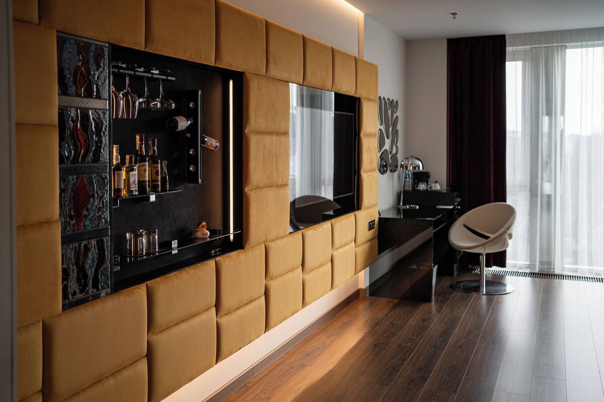 A modern living room with a large flat-screen TV mounted on a wall with a cushioned panel, a wooden floor, and a seating area with a chair.