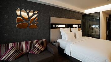 Una habitación de hotel moderna con una cama grande, un sofá con cojines a rayas, una lámpara de pared y un separador de vidrio.