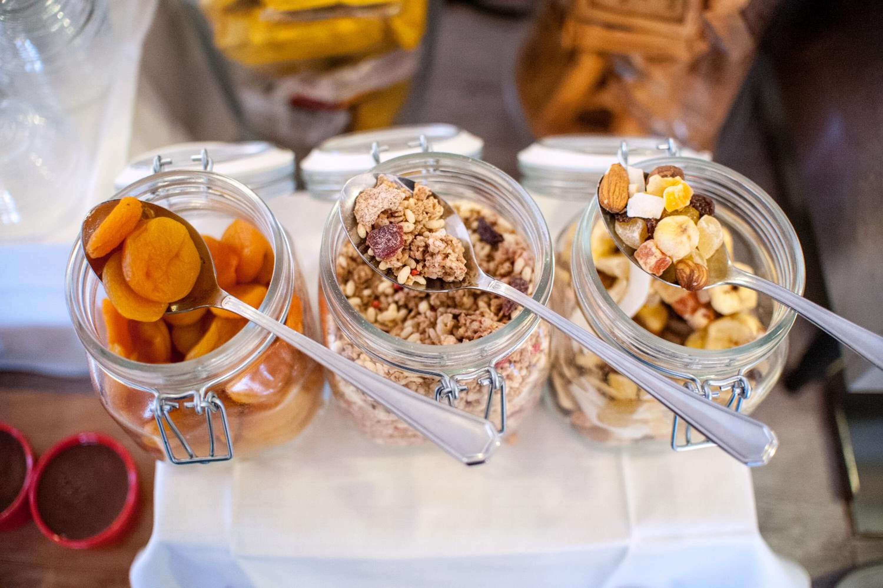 Trois bocaux en verre munis de fermetures métalliques, contenant différents types de granola et de fruits secs.