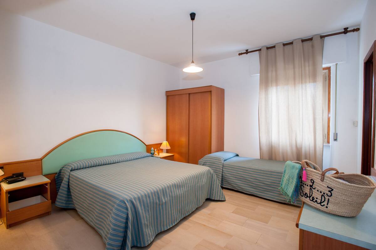 Une chambre d’hôtel avec deux lits, une armoire en bois, une table de chevet avec une lampe et un grand panier en osier.