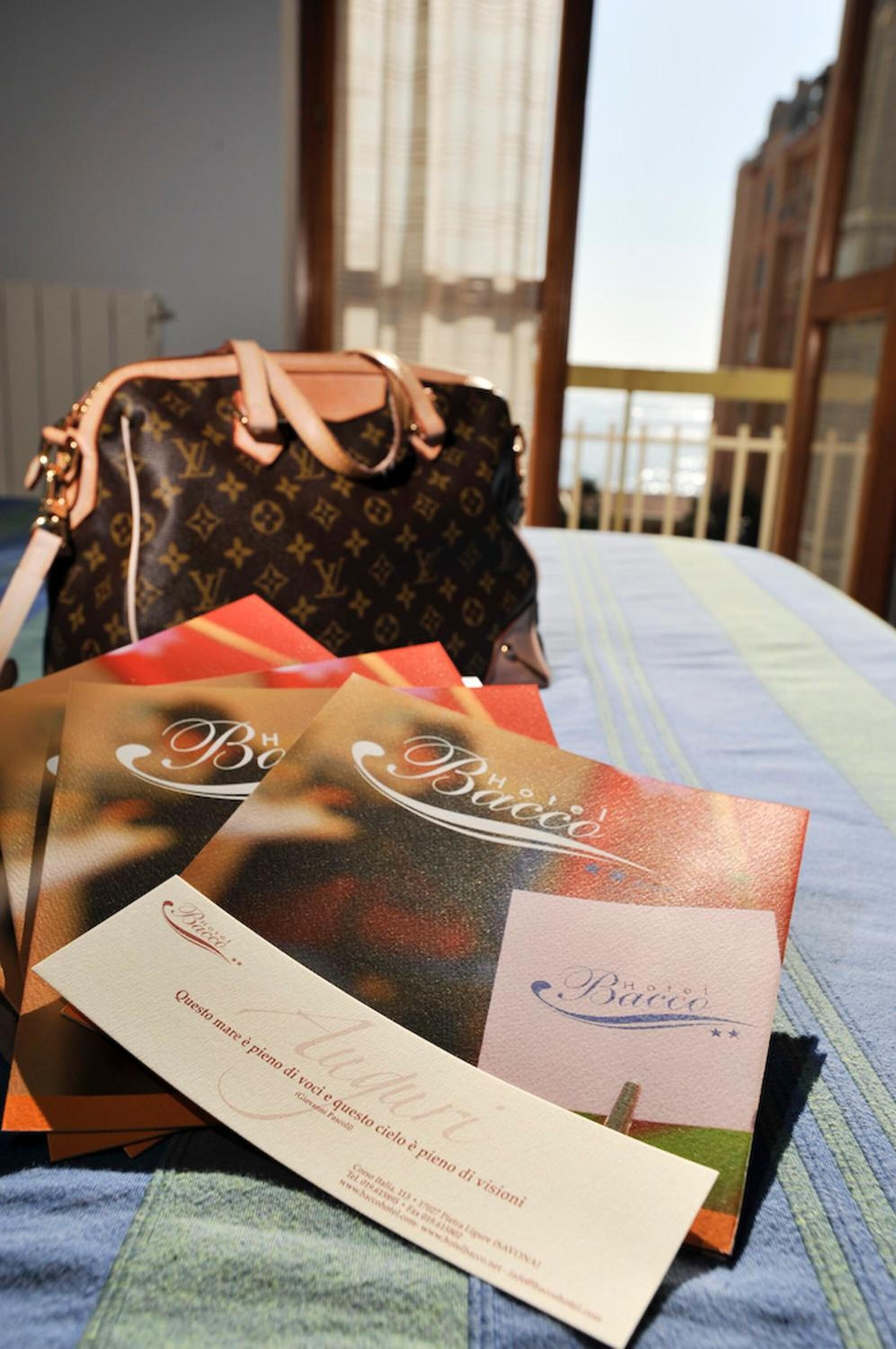 A bed with a striped bedspread, a Louis Vuitton bag, and several hotel brochures.
