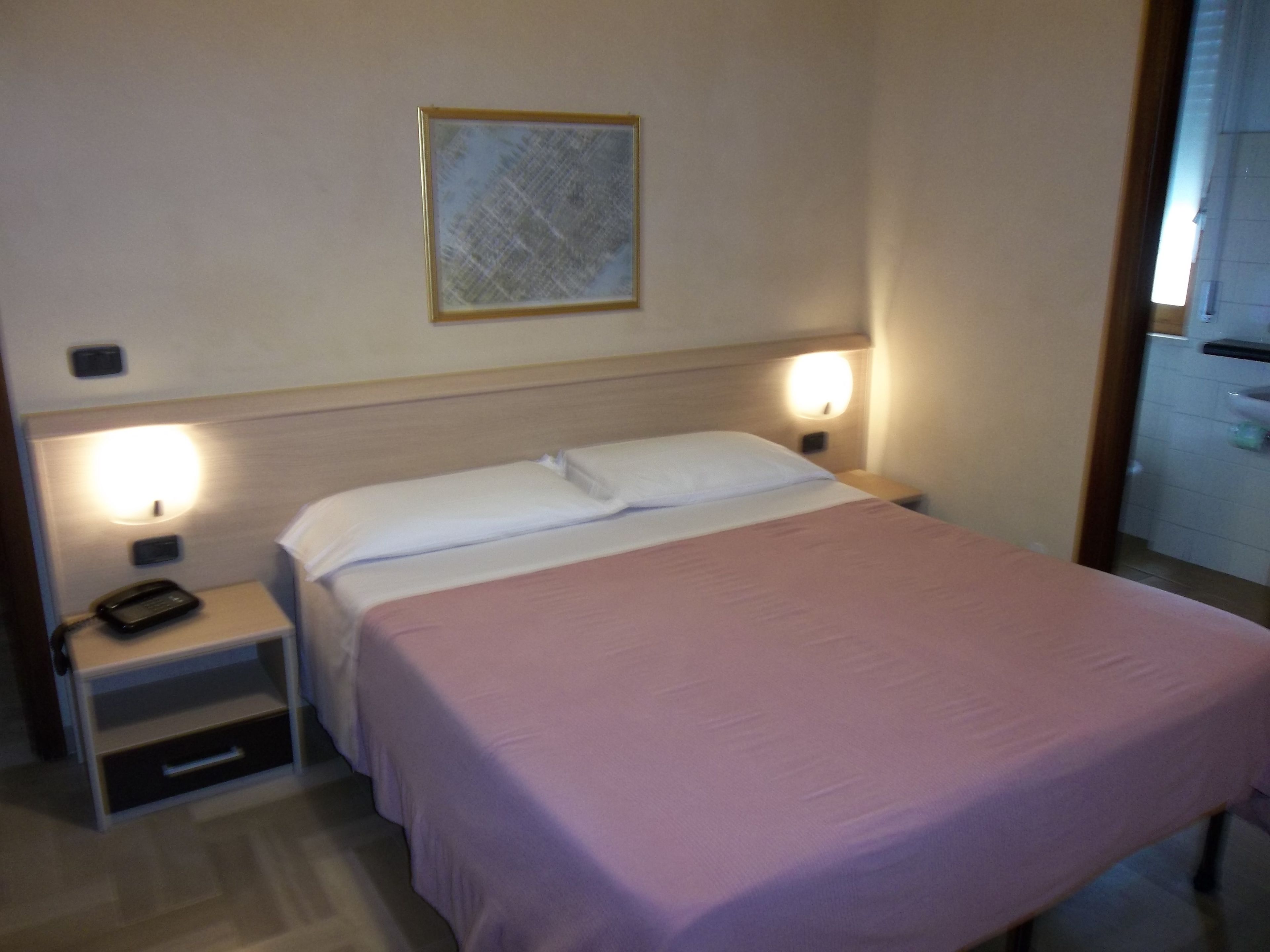 Een hotelkamer met een bed, bedlampen, een nachtkastje met een telefoon en een klein lade.