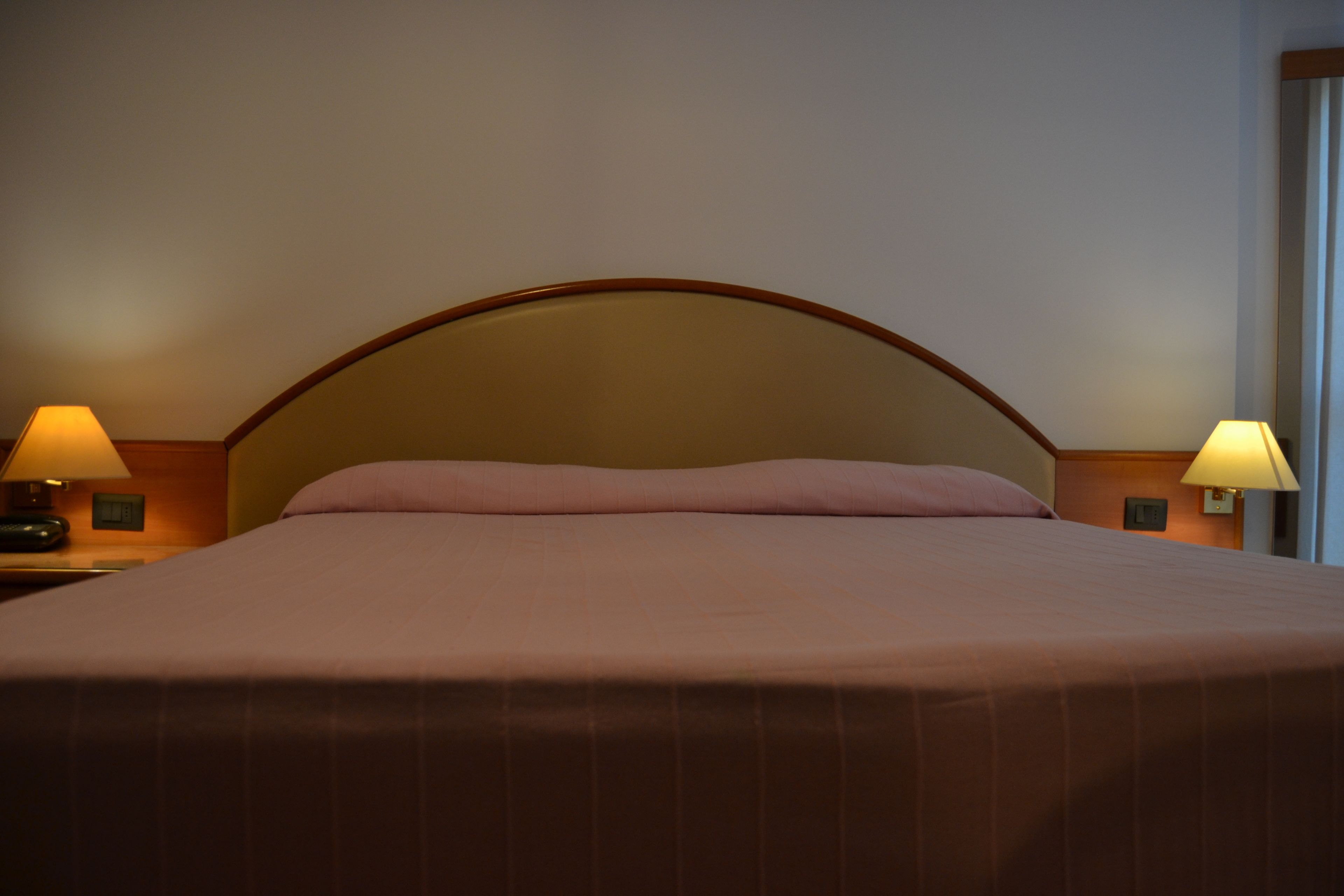 A neatly made bed with a headboard, two bedside lamps, and a nightstand.
