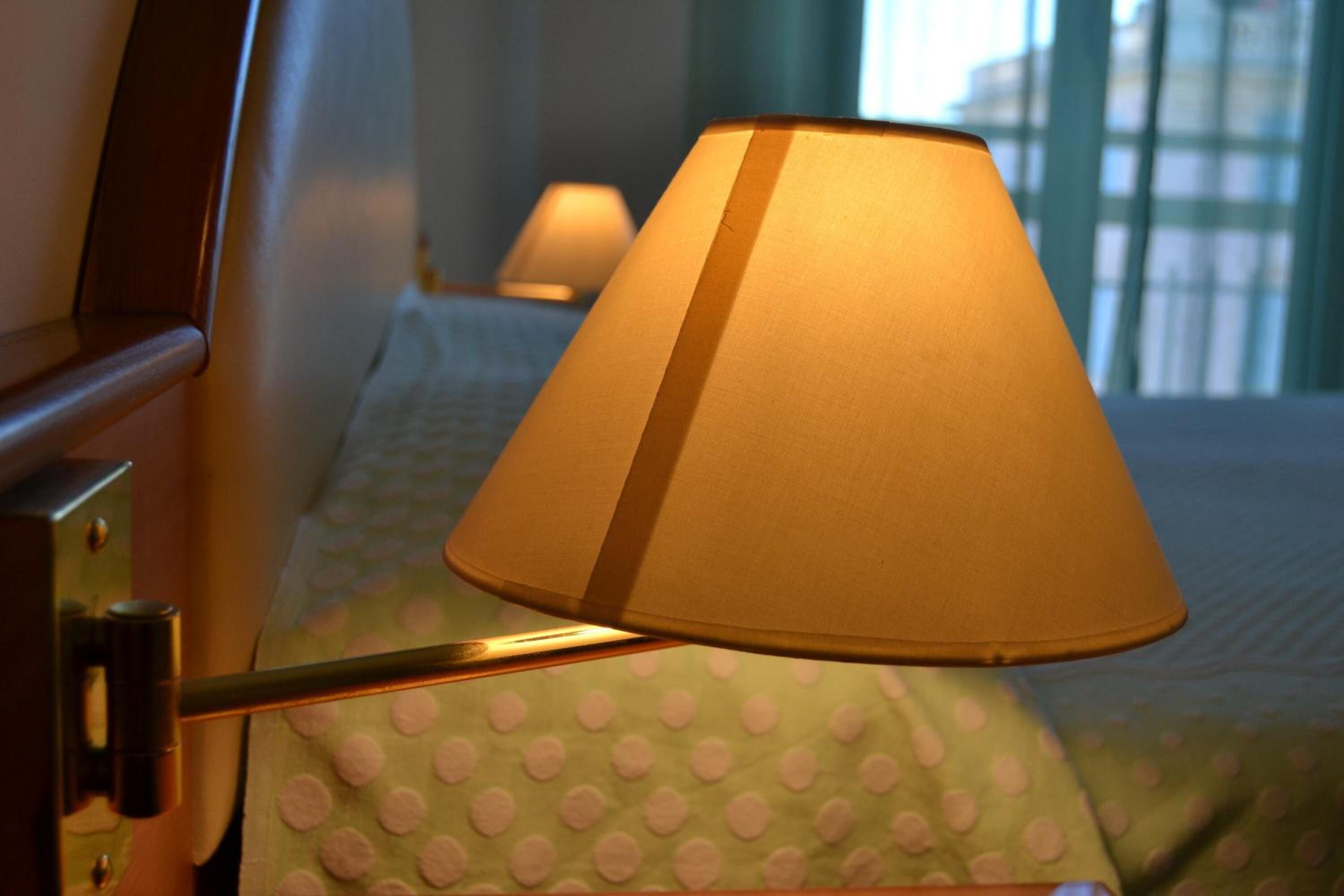 Ein Bett mit einer grünen Bettdecke mit Punkten und einer einzelnen Nachttischlampe.