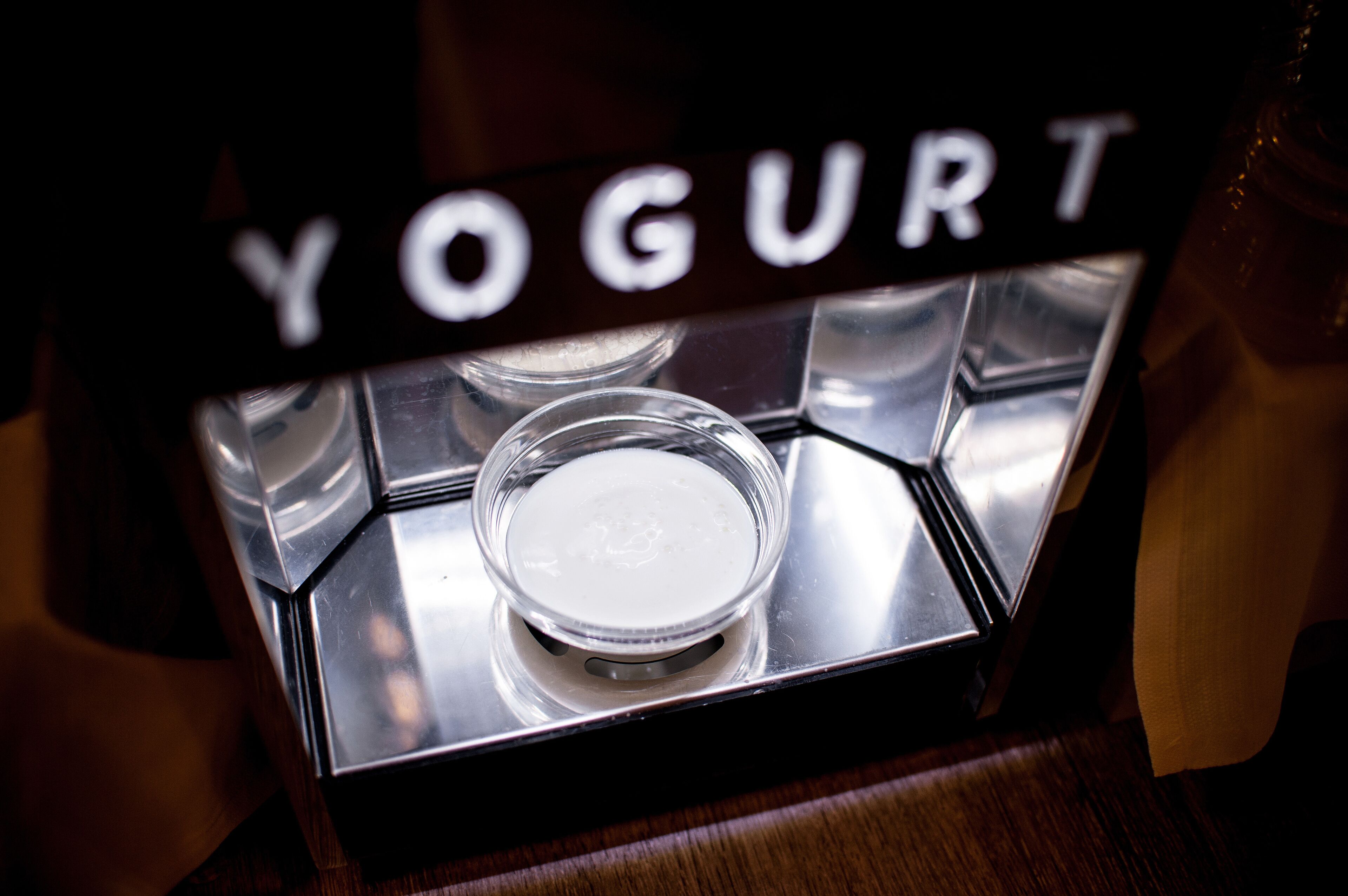 Een yoghurtbeker op een dienblad met een bordje er boven met de tekst 'YOGURT'.