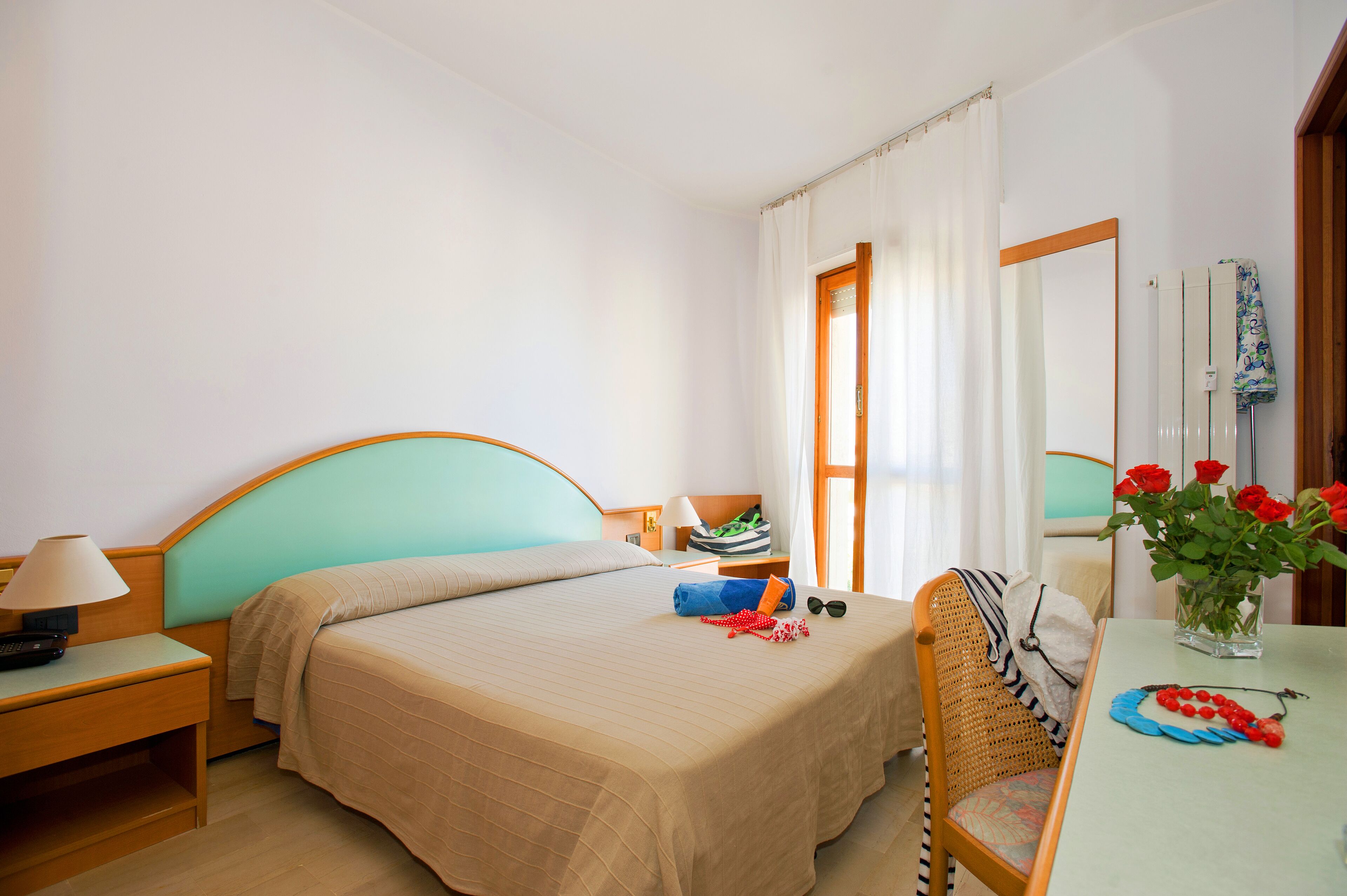 Ein Hotelzimmer mit einem Bett, einem Schreibtisch, einem Stuhl, einem Tisch und einer Blumenvase.