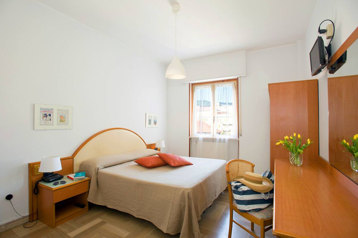 Une chambre à coucher avec un lit, une table de chevet, une lampe et une fenêtre avec des rideaux.