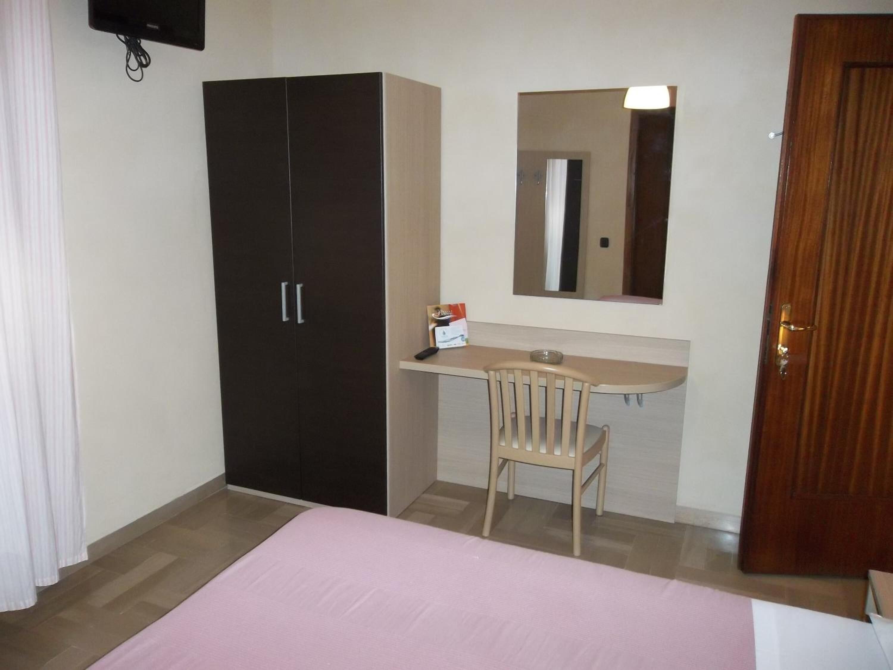 Un dormitorio con cama, armario, escritorio con silla, espejo y puerta.