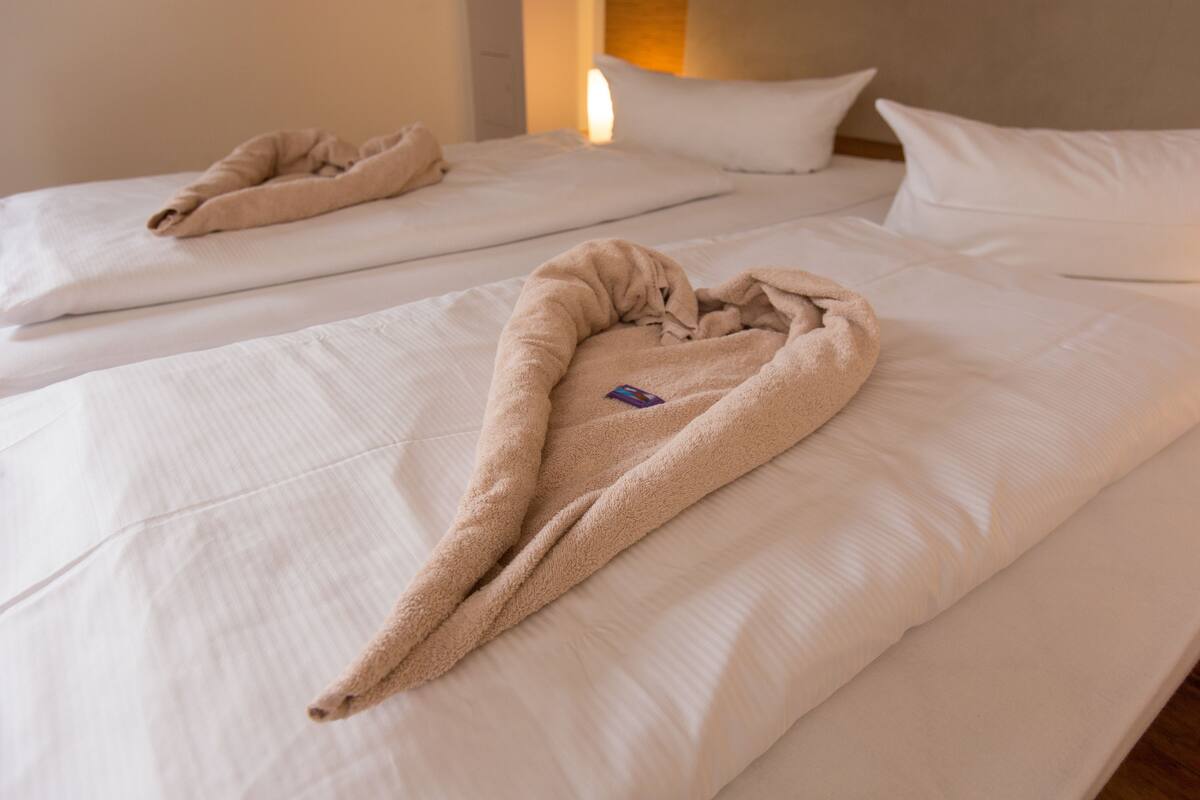 Two beds with white linens and a beige towel draped over one.