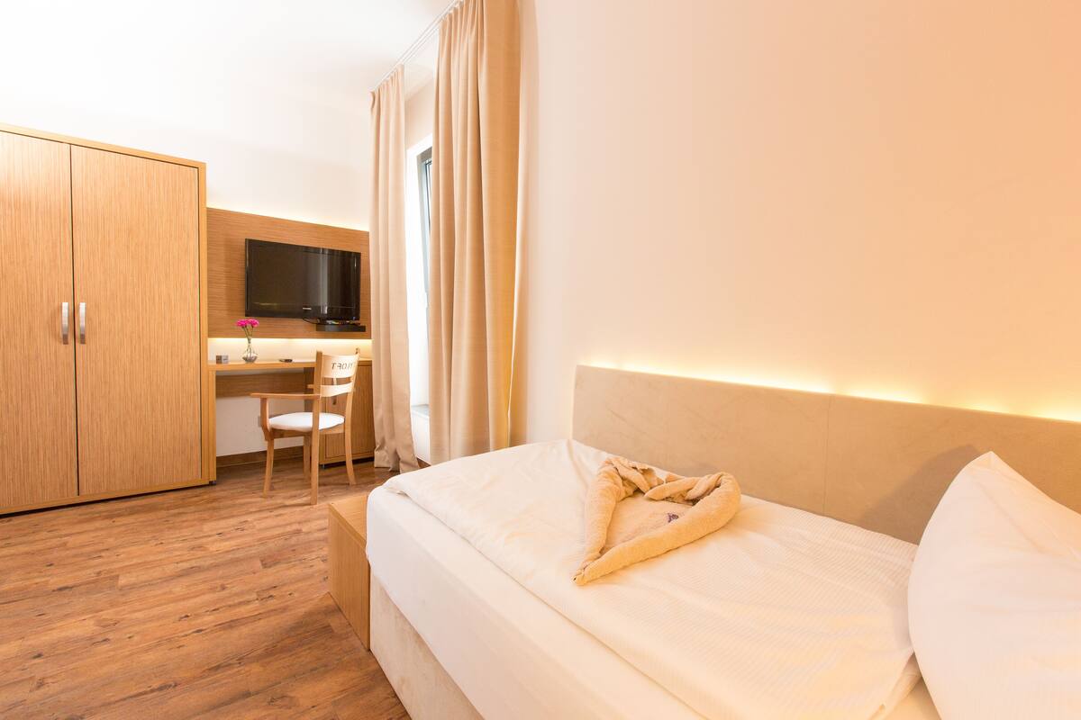 A hotel room with a bed, a desk, a chair, and a TV.