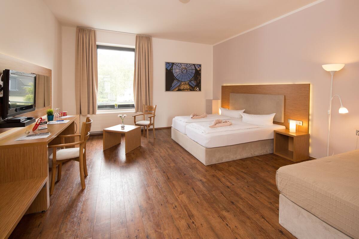 A hotel room with a bed, a desk with a chair, a television, and a window with curtains.