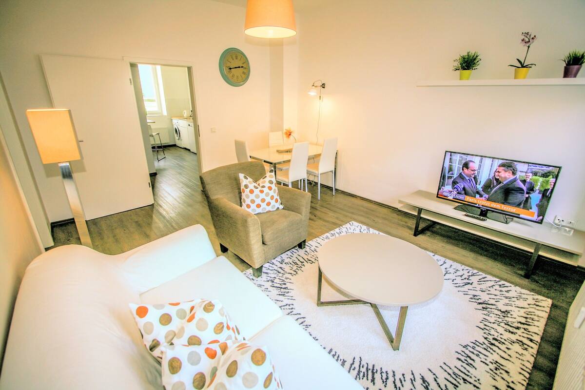 A living room with a sofa, a coffee table, a TV, and a dining area with chairs and a table.