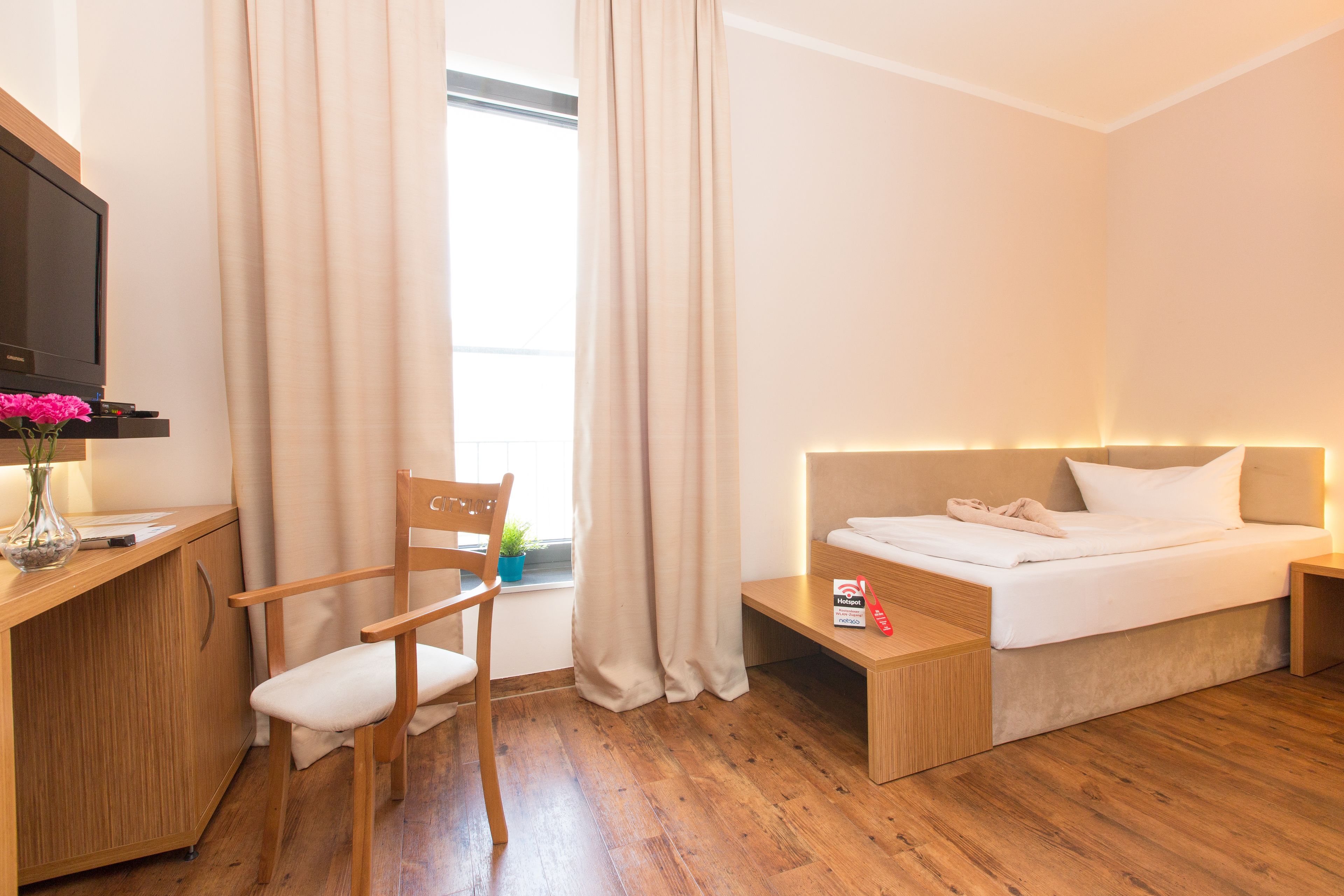 A hotel room with a wooden desk, a chair, a bed with a headboard, and a window with curtains.