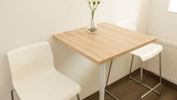 Quarto pequeno e moderno com uma mesa de madeira e duas cadeiras brancas.