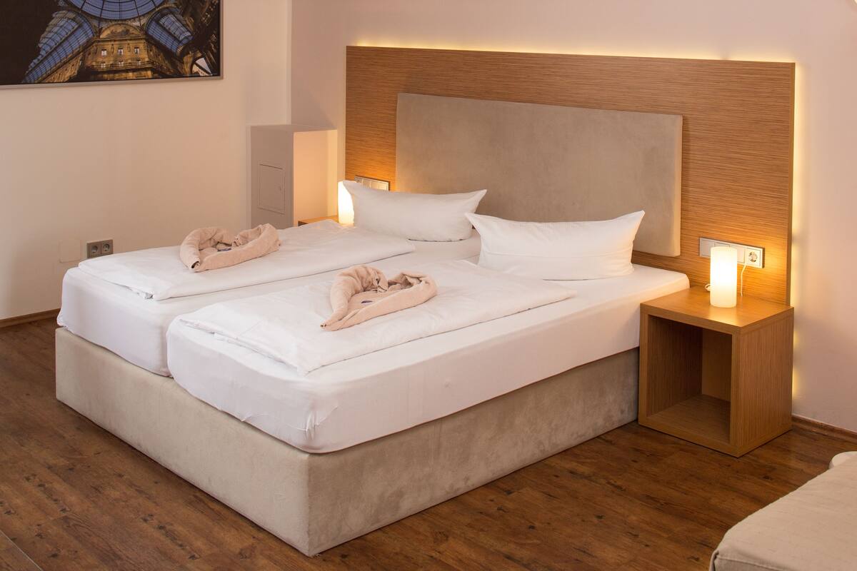 A double bed with white linens and a wooden headboard. There are two bedside tables with lamps.
