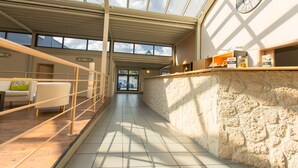 Amplio espacio interior con techo alto, ventanas grandes, pared de piedra y mostrador de recepción.
