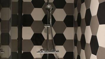 Ducha de diseño moderno, con pared de patrón geométrico y cabezal de ducha cromado.