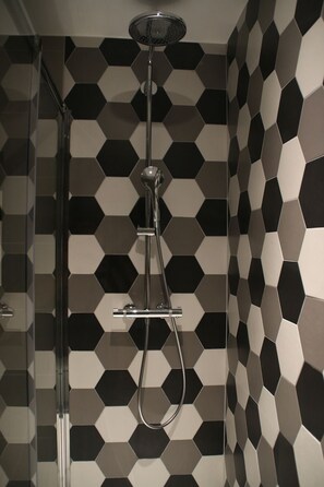 Une douche au design moderne, avec un mur orné d’un motif géométrique et une pomme de douche chromée.