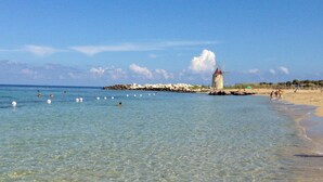 A beach with clear water, a windmill, and a rocky breakwater. - B&B La Casa di Paola (Trapani)
