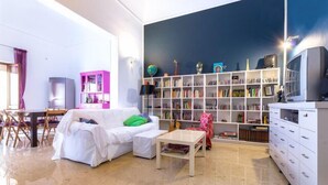 A living room with a white sofa, a coffee table, a bookshelf, and a television. - B&B La Casa di Paola (Trapani)